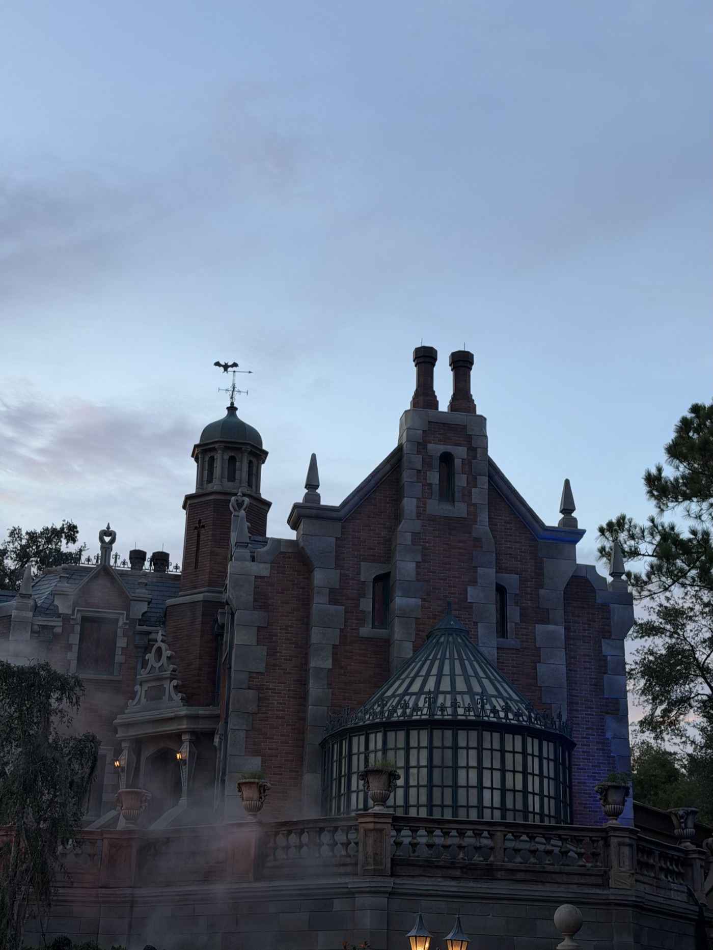The Haunted Mansion wrapped in fog at dusk on party night, bat weathervane and all